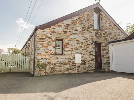 Stone exterior wall of a house with a wooden door and window next to a white garage door and a green wooden gate at The Wagon House Tresmeer near Launceston