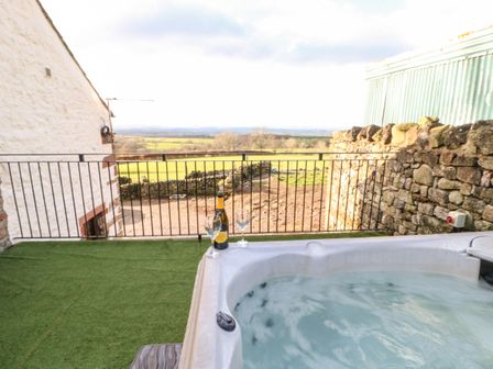 An outdoor hot tub with a bottle and two glasses on the edge overlooking a rural landscape at Rum Bush Cottage in Keisley near Dufton