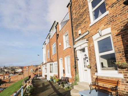 A row of brick houses with white doors and windows along a street with benches and plants at Overton Terrace in Scarborough
