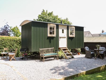 A green shepherds hut with white door and windows surrounded by outdoor seating and gravel at Shepherds Hut in Castleton Peak District