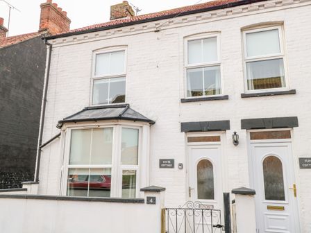 Front facade of a white brick cottage with two doors and three windows at White Cottage in Sheringham