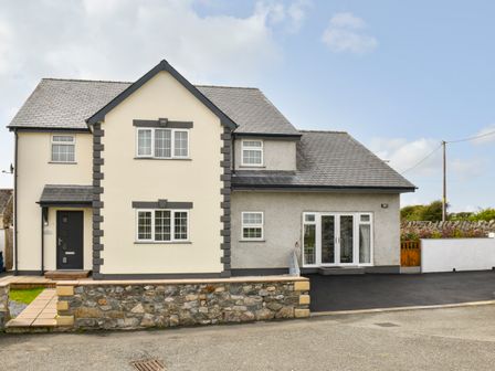 A detached house with white and grey walls a tiled roof and a stone wall in front at Plas Bach in Aberffraw