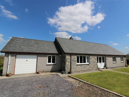 A single-story house with a stone and pebble dash exterior under a blue sky at Pen Y Cae in Llansannan