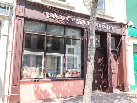 Front view of a shop with a large window display and a door on the right side with a tree in front at The Merchant's Store in Kilrush Country Clare