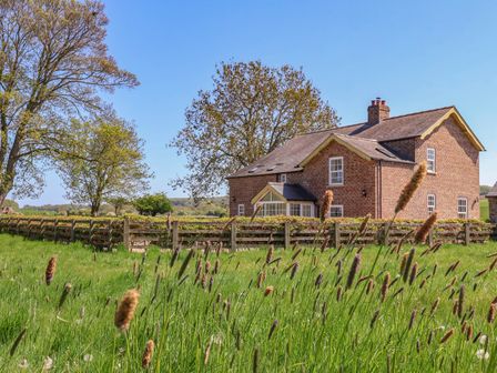 A brick house with a wooden fence and tall grass in the foreground at Foremans House in Bridlington