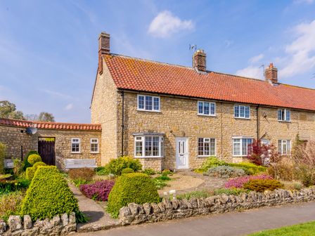 A stone cottage with a red tiled roof and manicured garden at Ivy Cottage in Helmsley