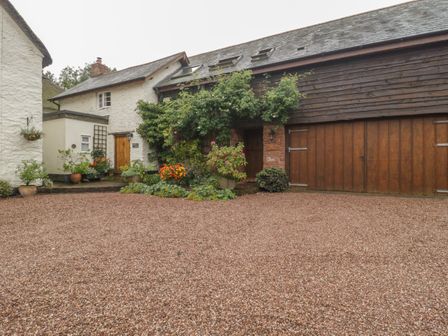 An outdoor courtyard area with gravel ground plants and a white stone building with wooden doors at The Old Bakery in Crowcombe