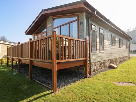 A single story house with wooden porch railing and multiple windows on a grassy area at Tranquillity - Heritage Park in Stepaside near Kilgetty