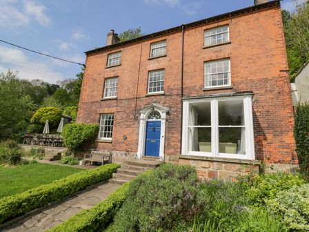 A brick house with a blue front door surrounded by bushes and a garden with a stone pathway at Viaduct House in Lydbrook
