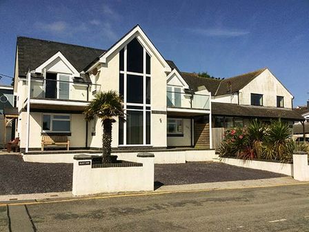 A modern two story house with large windows and a palm tree in front at Glan Y Mor in Bull Bay
