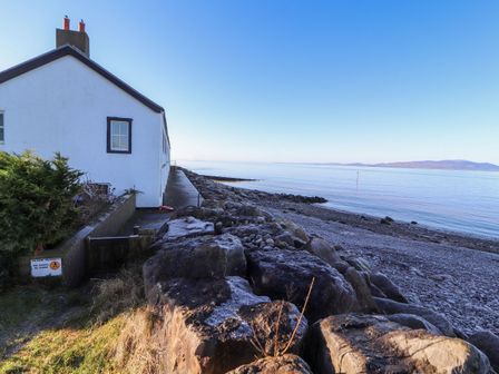A coastal scene with a white house next to a rocky shore and calm sea at Greenmantle in Skinburness near Silloth Solway Firth