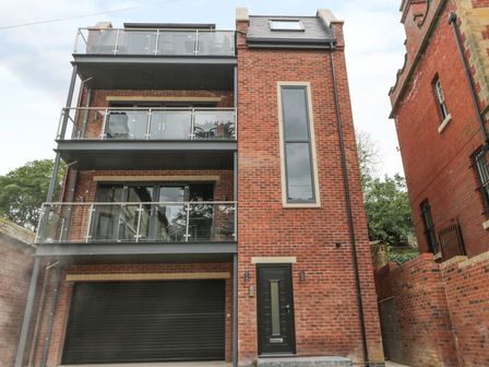 A modern three-story brick building with glass balconies and a black garage door at The Office Gardens Apartment 1 in Whitby