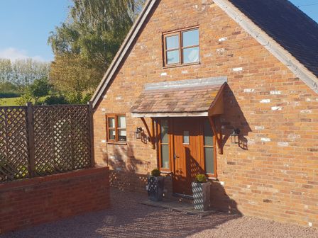 A brick house with a wooden door and two small windows at Woodstock Lodge in Suckley