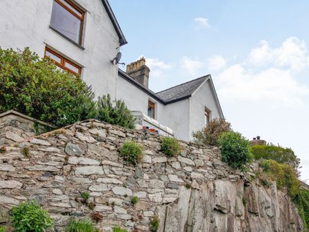A white building with a stone wall and shrubs in front at Pen Y Graig in Talysarn