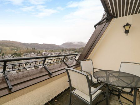 An outdoor balcony with a metal table and four chairs overlooking a town and hills at Rothay 17 in Ambleside
