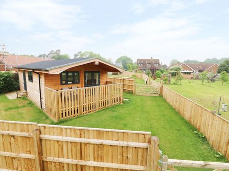 A wooden cabin with a fenced porch and a grassy backyard at Hayfields in Grimston