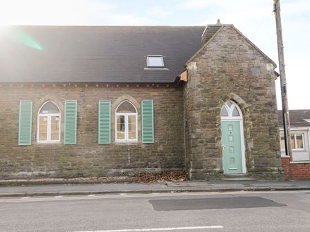 A stone building with arched windows with green shutters and a green door on a street at No 1 Church Cottages in Llanelli