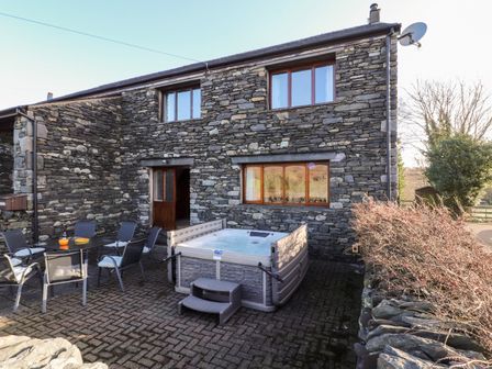 An outdoor patio area with a hot tub and a table with chairs beside a stone house at Green Hills Farm in Ulverston