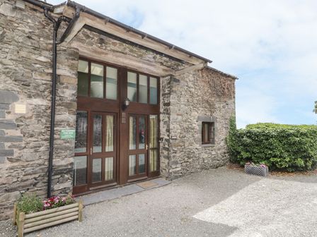 Stone building with wooden double doors and small window with planters and hedge at Bank End Barn in Grizebeck