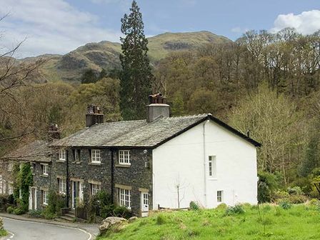 A row of stone and white cottages near a curving road with hills and trees in the background at Littlebeck Seatoller near Rosthwaite and Keswick