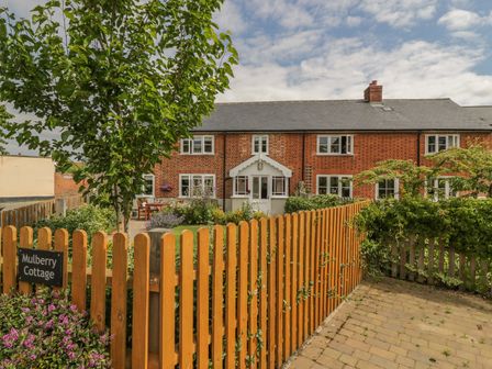 A brick cottage with white windows and a wooden fence with a gate and garden at Mulberry Cottage Hadleigh near Ipswich
