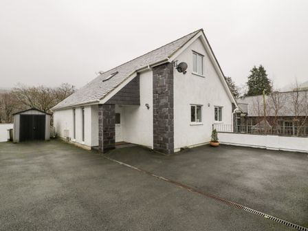 An exterior view of a white house with dark stone pillars and a pitched roof with a small shed on the side at Ty Coch in Llanberis