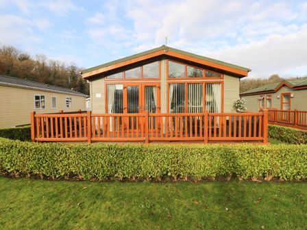 A single story cabin with a wooden deck and hedges in front at The Retreat in Wisemans Bridge near Saundersfoot