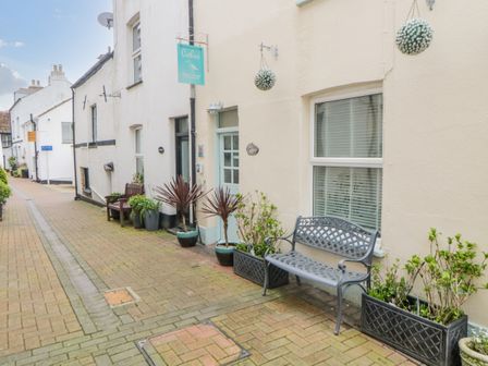 A narrow paved street with a bench and potted plants outside a cream colored building at Curlews Cottage in Looe