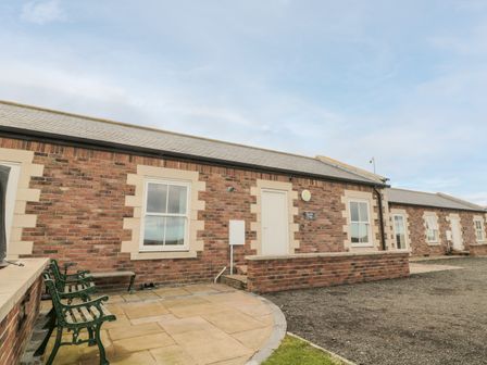 The exterior of a single story brick building with benches on a paved area at Bank Top Cottage in Embleton