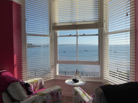 A sitting area with two armchairs and a small side table by a window overlooking the sea at 1 Beachtop Court in Tenby