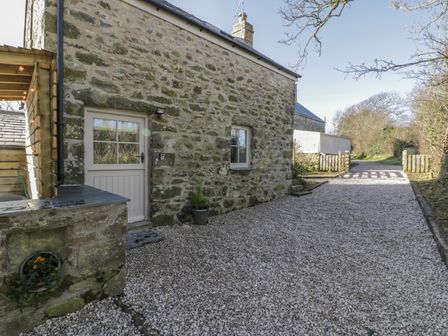 A gravel driveway leading to a stone house with a white door and window at Owl Cottage in Abersoch