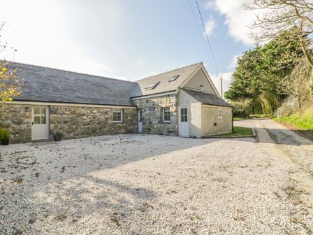 A stone house with a gravel driveway and surrounding trees at Horseshoe Cottage in Abersoch