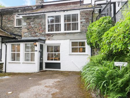 Exterior view of a stone and white painted house with windows and a black door next to greenery at Ramblers Roost in Grasmere