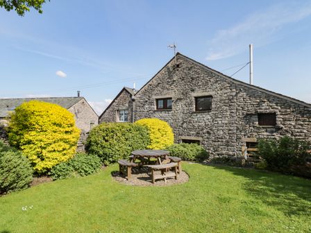 A stone house with a garden and round wooden picnic table with benches at Riven Oak in Lyth Valley near Levens