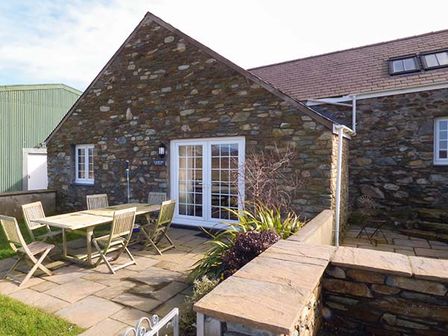 An outdoor patio with a wooden table and chairs next to a stone building at Y Barcud in Holyhead