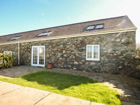 An exterior view of a stone house with white framed windows doors and a grassy yard at Y Wennol in Holyhead