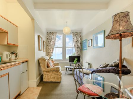A small living room with chairs a glass dining table a kitchen area and a window with a view of the ocean at Clooneavin Apartment 5 Lynmouth near Lynton