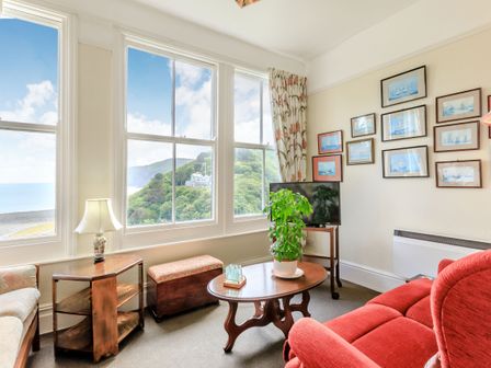 A sitting room with large windows showing a coastal view a red armchair a coffee table with a plant a TV and framed pictures on the wall at Clooneavin Apartment 6 in Lynmouth near Lynton
