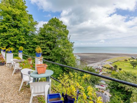 A terrace with white plastic chairs and tables overlooking a rocky beach and the sea at Clooneavin Apartment 8 in Lynmouth near Lynton