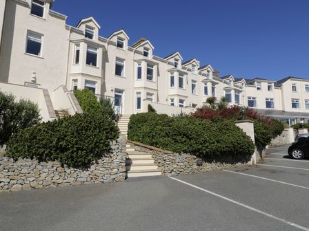 Exterior view of a multi-story white building with multiple windows stairs in front and parked cars at Trearddur Views in Trearddur Bay