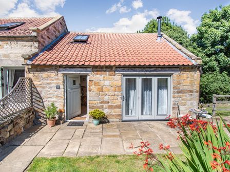 Exterior view of a stone cottage with a red tiled roof a half-open door two potted plants and a patio area with garden furniture at Cottage Anton in Ravenscar