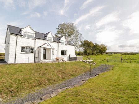 A white two-story house with dormer windows and outdoor seating on a grassy lawn at Bryndan in Machynlleth