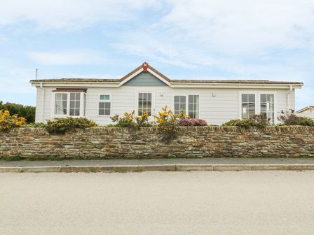 A single story white house with multiple windows behind a stone wall with plants at 11 Pendarves St Merryn near Padstow