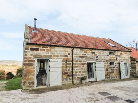 A stone building with a red tiled roof and white wooden doors and shutters at Cottage Val in Ravenscar