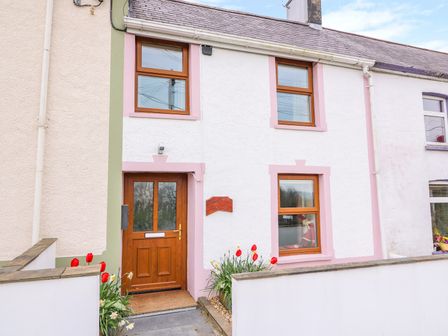 The front of a two-story house with a wooden door and brown framed windows with red and white flowers planted outside at Bank House in Capel Iwan near Newcastle Emlyn