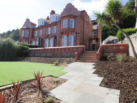 A brick building with stairs leading to an entrance and a garden path at Tan Tabin in Llandudno
