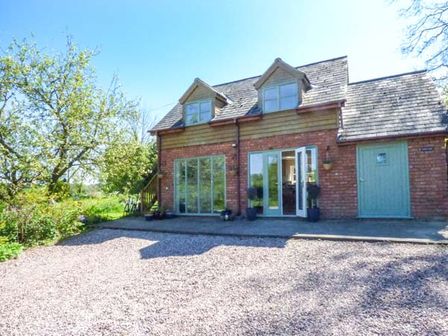 A brick house with two dormer windows and glass doors on a gravel driveway at Gwdihw in Gobowen