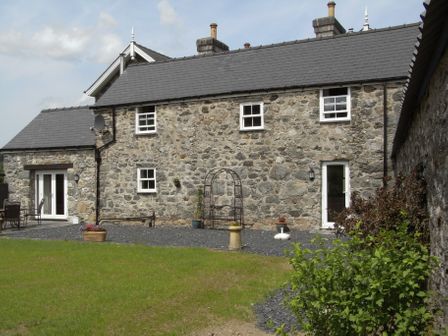 A stone house with white-framed windows and doors surrounded by a garden and patio at Y Bwythyn at Henfaes in Rhydymain near Dolgellau