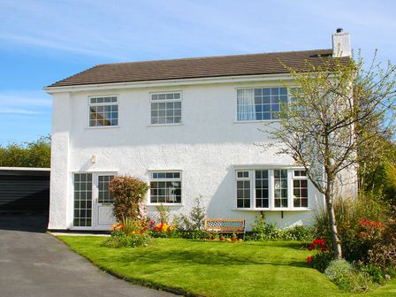 A two story white house with windows a garden bench and flowers in the front yard at Anglesey White Haven in Llandegfan near Menai Bridge