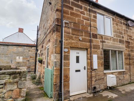 Stone built cottage with a white door numbered 50 and windows at Mill Cottage in Hinderwell near Runswick Bay